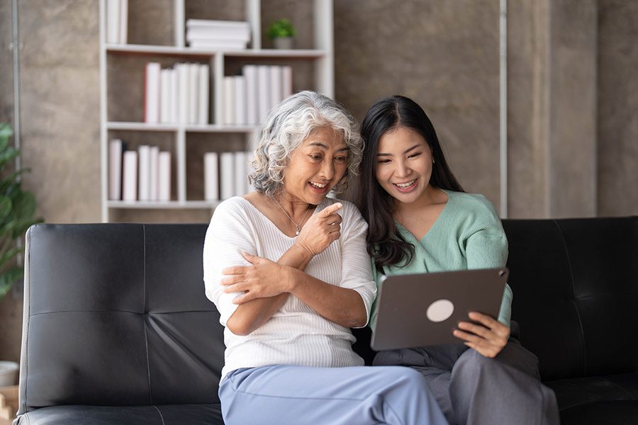 Blog - Grandmother and Grandaughter Looking at a Tablet Together on the Sofa and Smiling